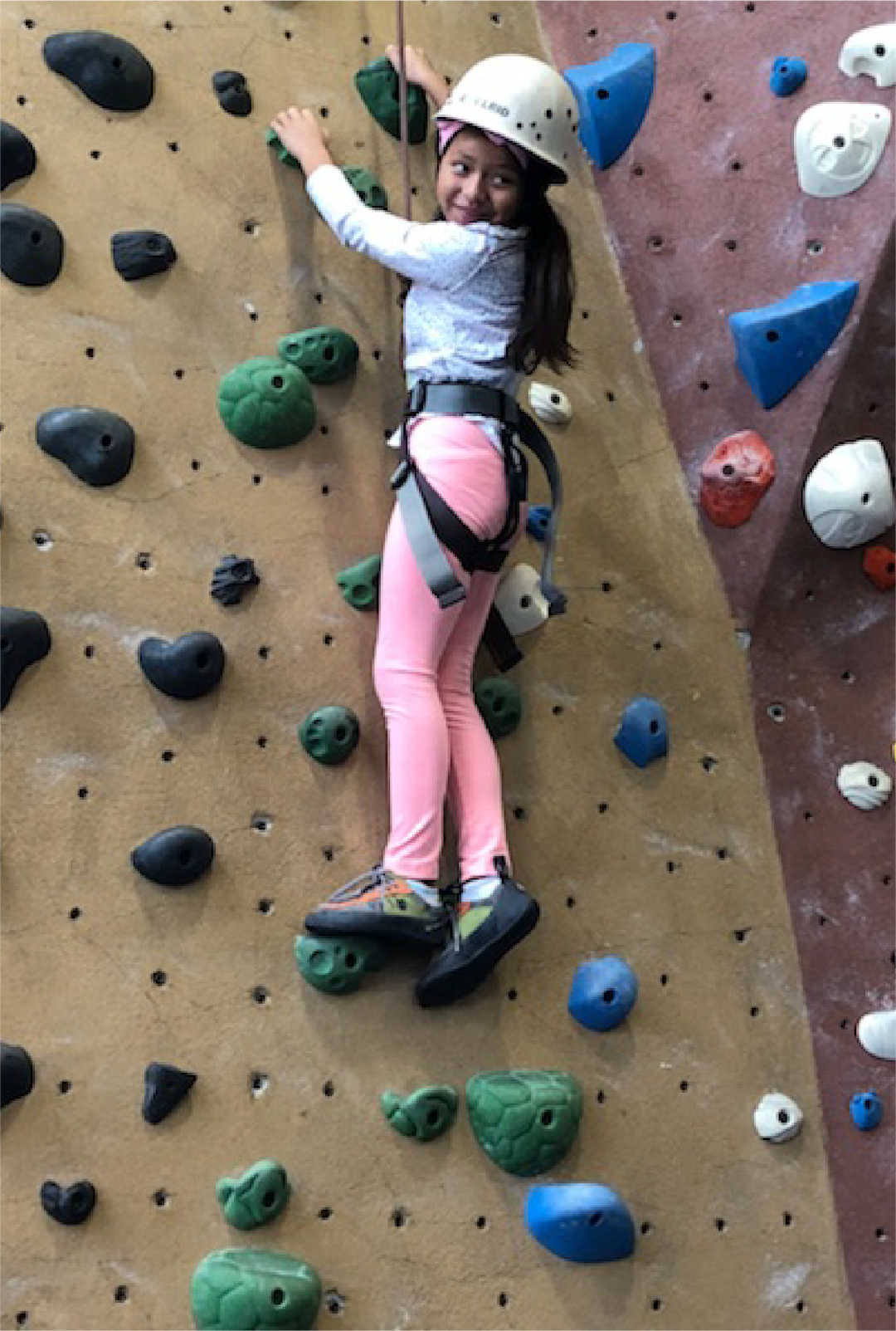 A young girl ascends a rock-climbing wall