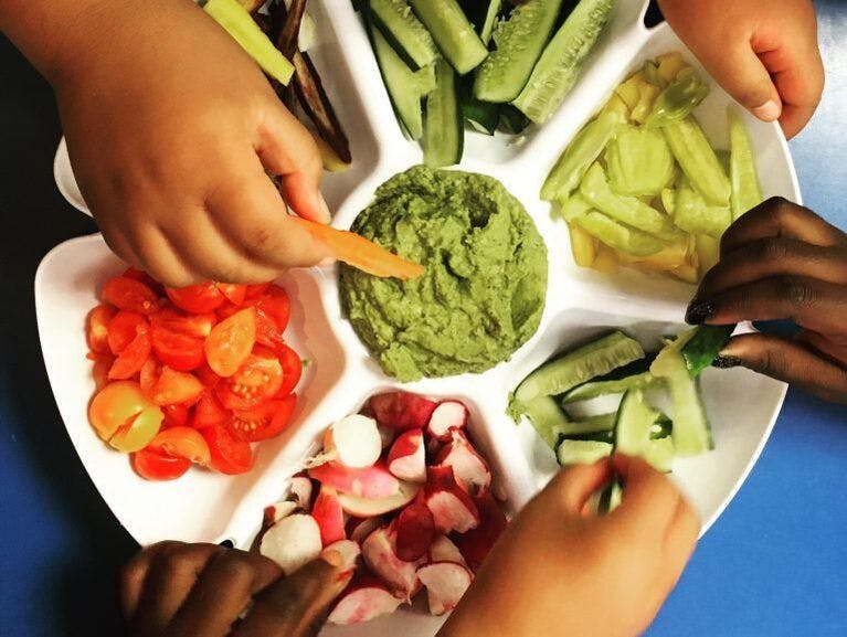 Children's hands reach for healthy fruits and vegetables on a platter